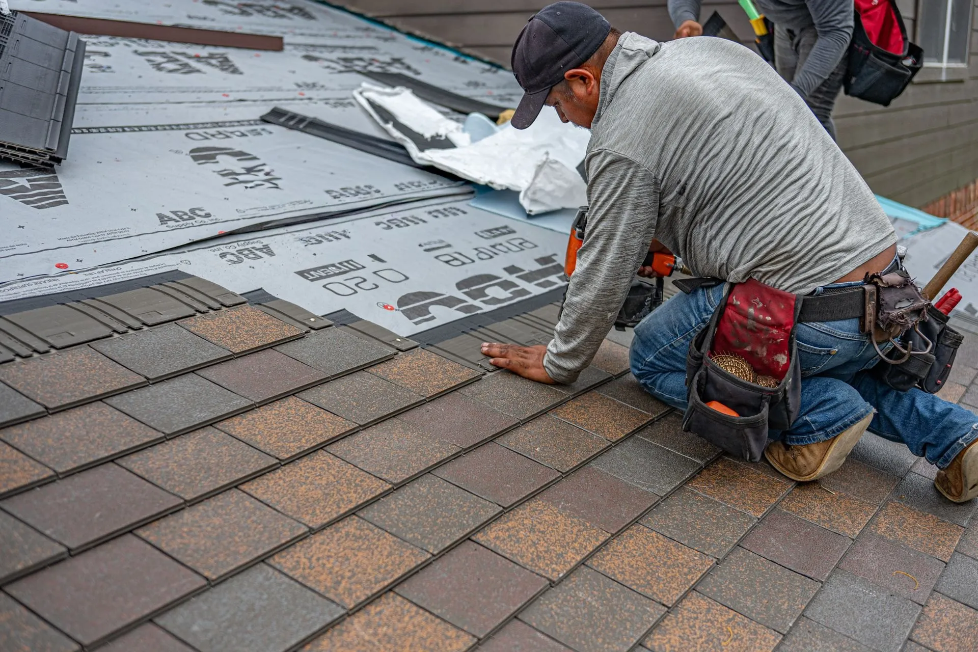Roofer nailing new asphalt shingles into place on a residential roof