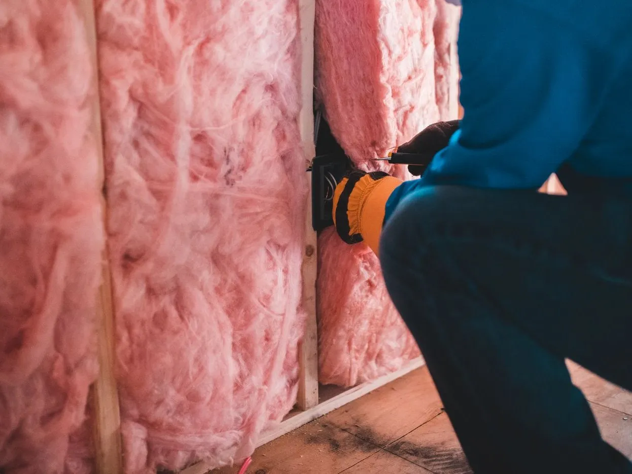 Worker installing pink fiberglass batt insulation in an attic wall