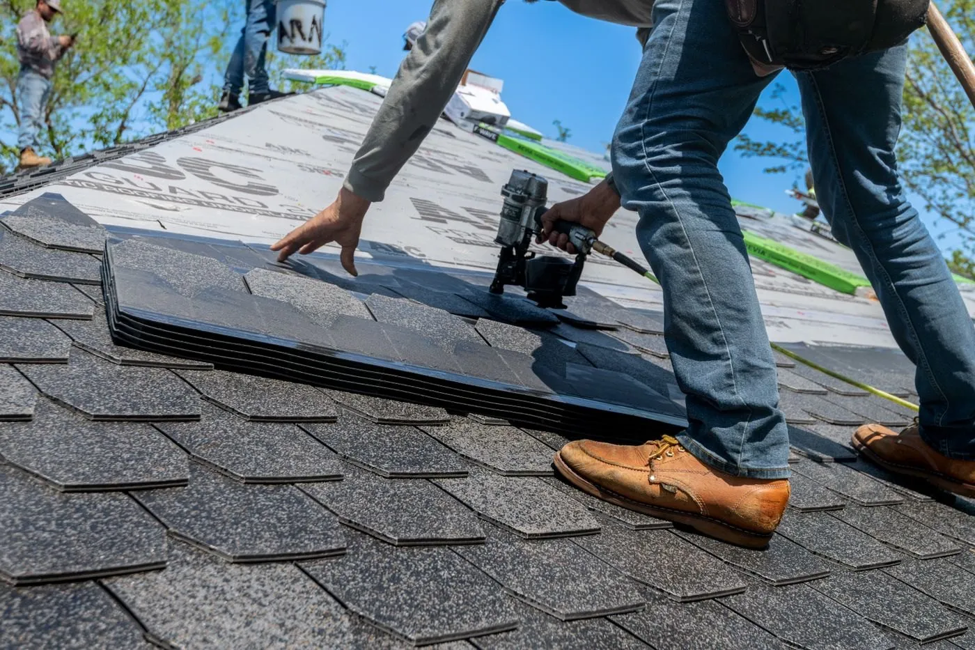 Roofer using a pneumatic nail gun to install shingles on a roof deck