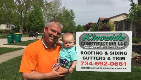 Scott Kincaide holding his son beside a Kincaide Construction yard sign outside a Westland, MI job
